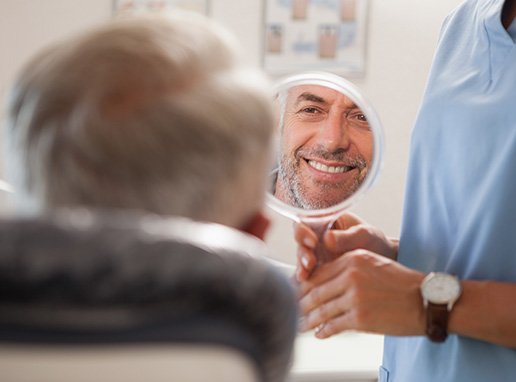 Man smiling while looking at reflection in handheld mirror