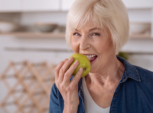 Woman eating an apple after dental bridge tooth replacement
