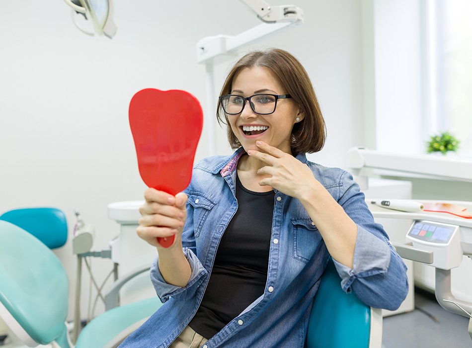 Woman looking at smile in mirror after dental checkup and teeth cleaning visit