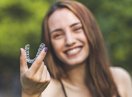 Smiling woman holding a clear correct clear aligner