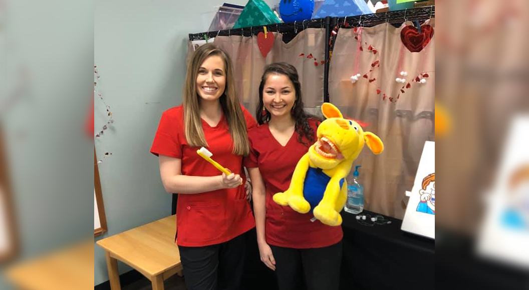 Two dental team members with tooth brushing puppet at community event
