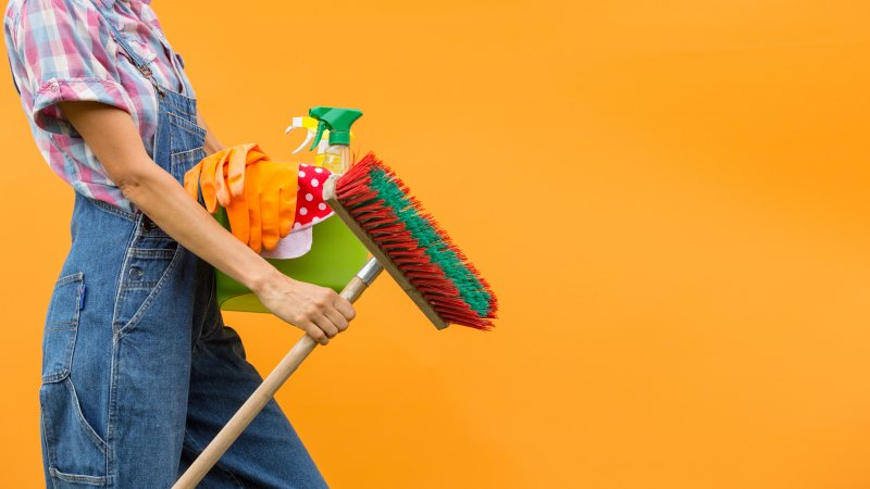 woman in overalls carrying cleaning supplies