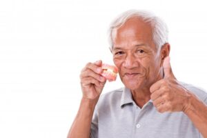 Older man holding dentures and giving thumbs up. 